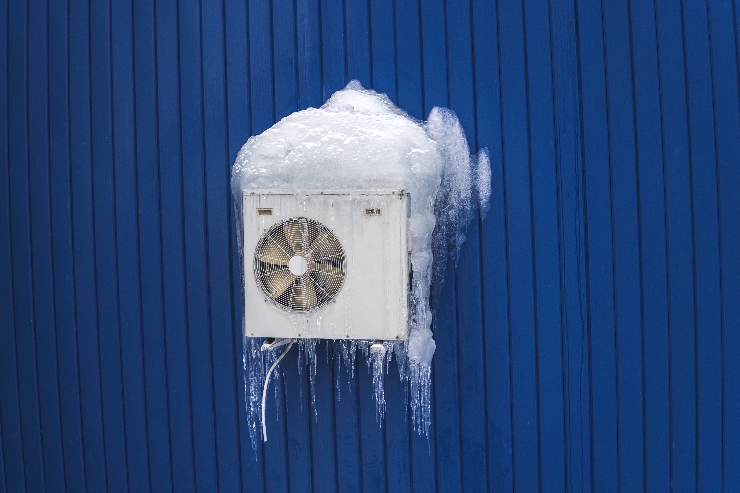 White AC Unit On A Blue Wall Covered In Ice