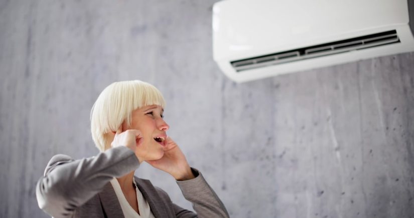 Photo of the woman standing next to air conditioner holding her ears