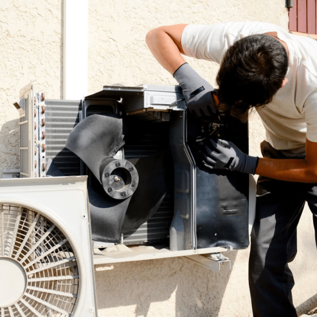 A technician repairing the internal components of an outdoor air conditioning unit