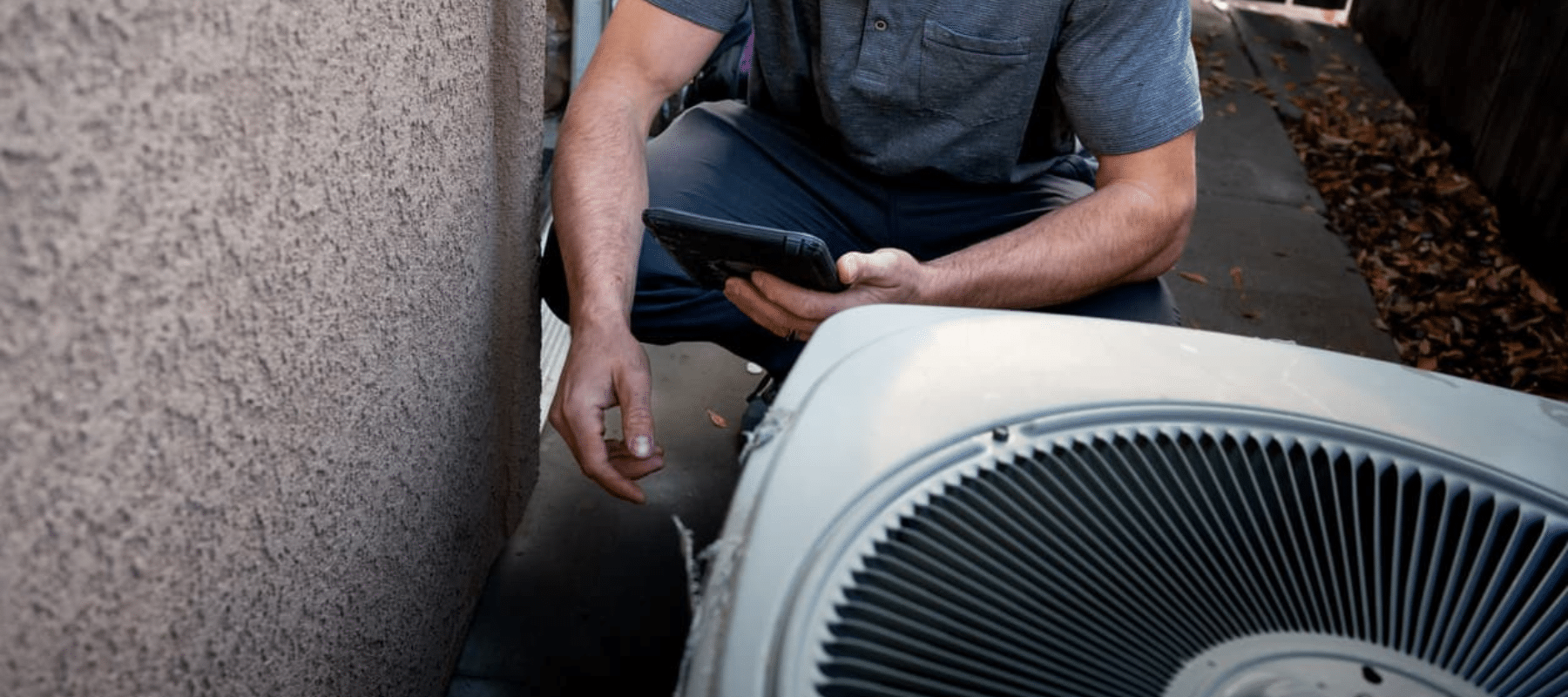 A technician inspects an outdoor air conditioning unit with a handheld device