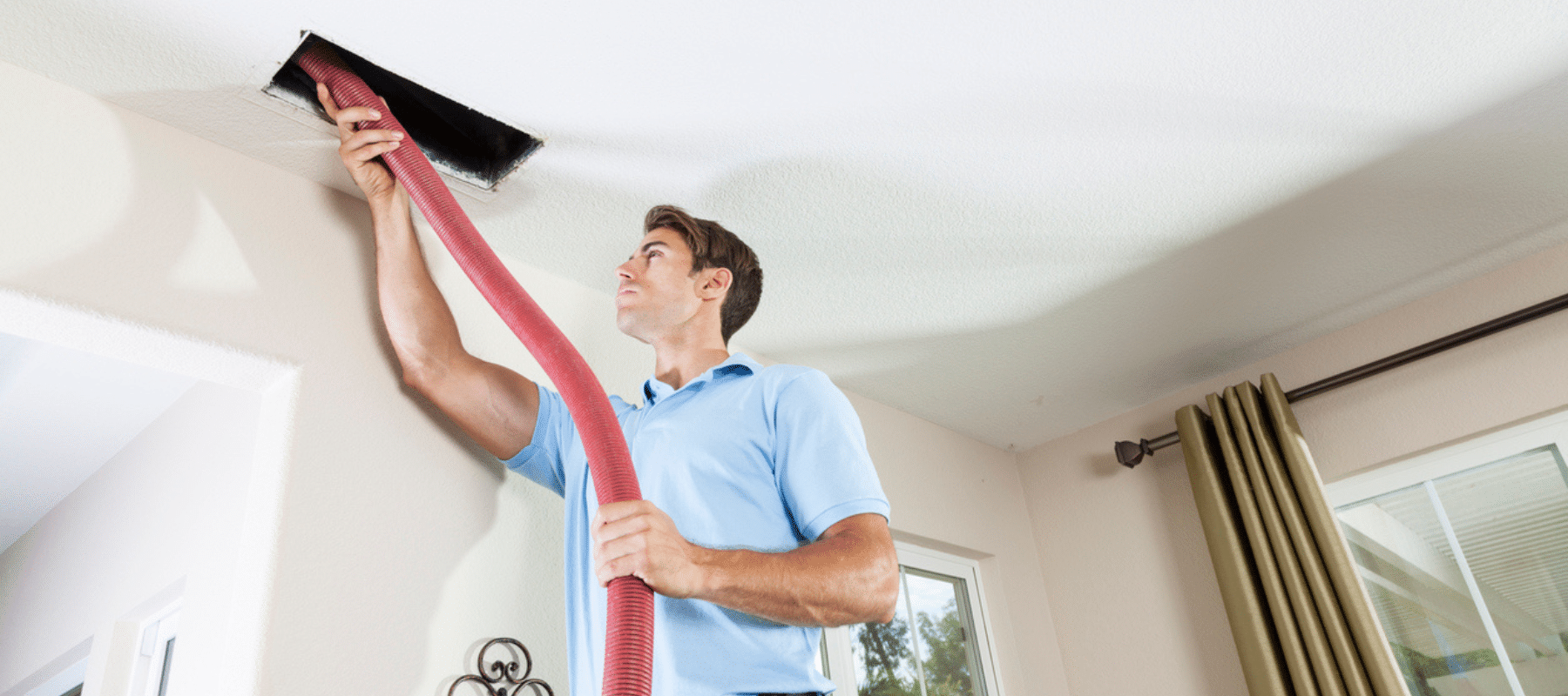 A worker cleans a home's air duct using a long red hose