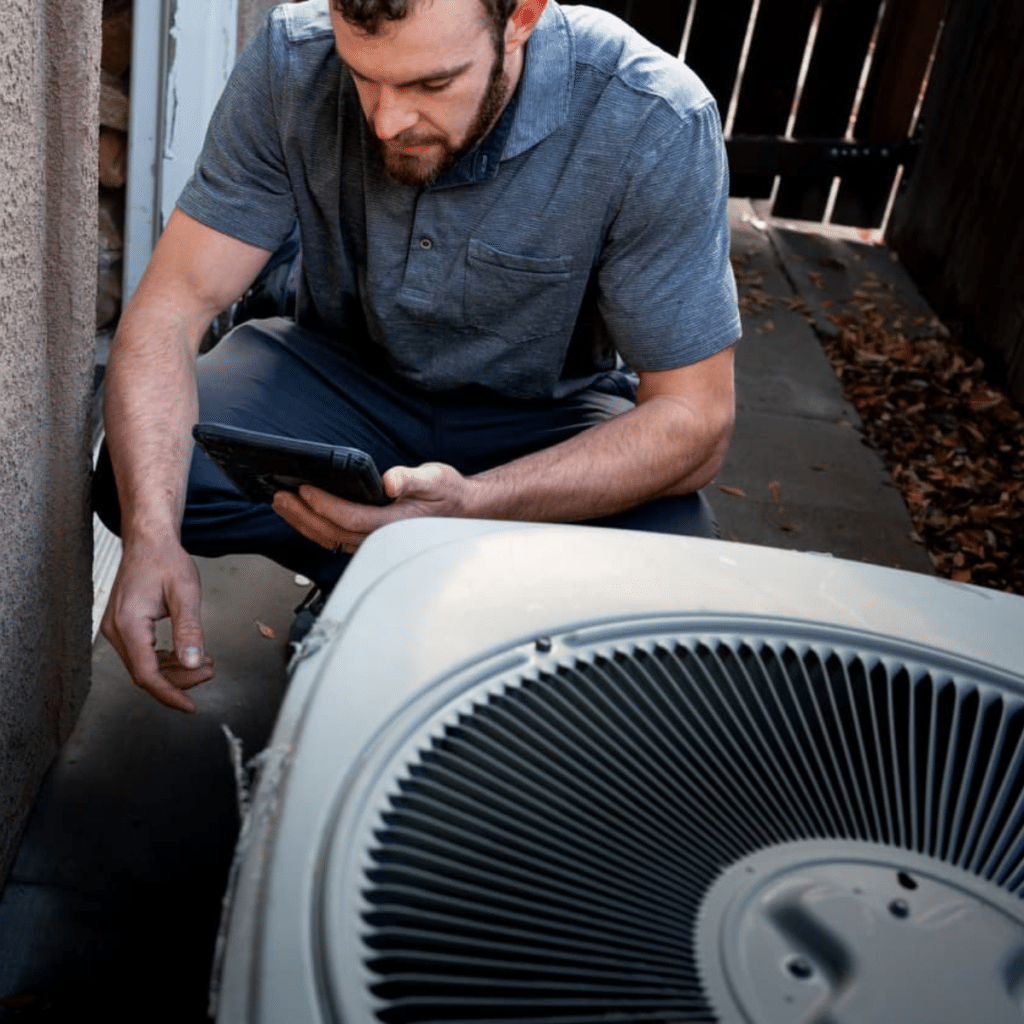 A technician inspects an outdoor air conditioning unit with a handheld device